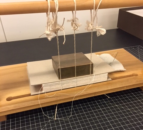 A book’s textblock being sewn over cord in a sewing frame