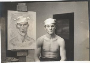 Photo of a model sitting next to a portrait of himself painted by Emlen Ettings. Date, title unknown., and photographer unknown.