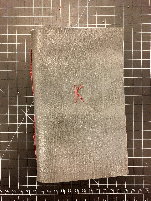 Hand-made book, bound in grey goatskin with red letter K stiched on cover.