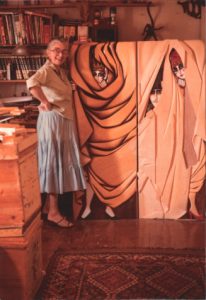 Image of Whitney Kent standing in front of one of her wooden sculpture pieces.