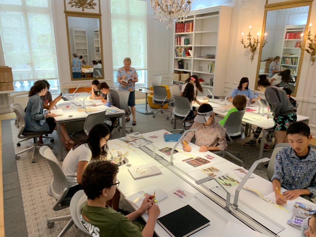 This image features group of Design Campers sitting in the library looking at books on shoes.