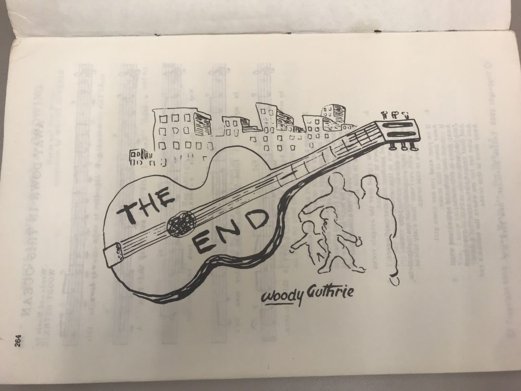 Black and white illustration of guitar with "The End" written on it, in foreground with city scene. 