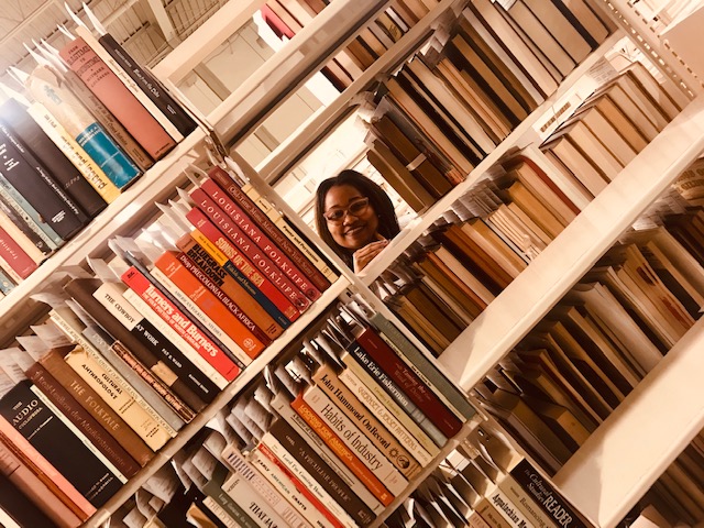 Intern Angela Brooks peering through space in book shelves.