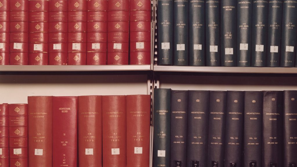 Color photograph of book spines on shelf, half red, half navy blue. 