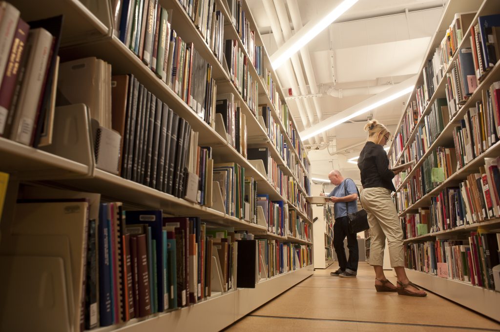 Photograph of two people looking at books on library shelves. 