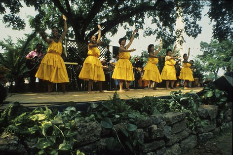 Six hula dancers in yellow dresses dance on stage.