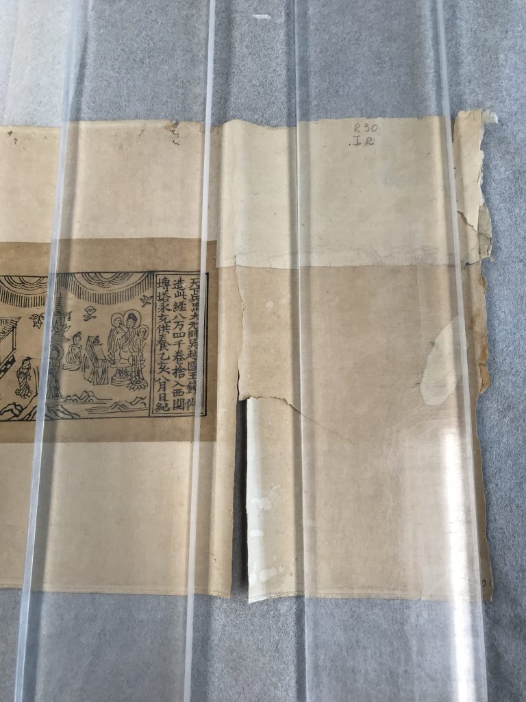 Damaged Chinese sutra scroll with tear. Scroll is under clear acrylic.