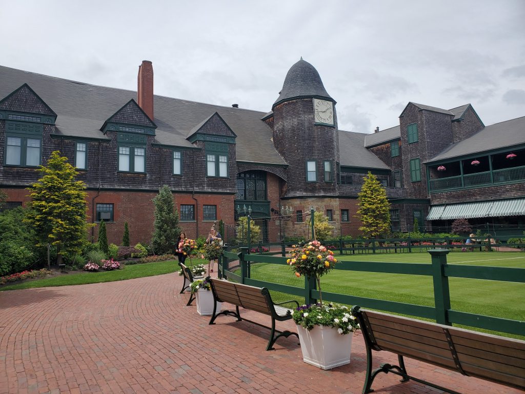 Fenced manicured lawn with two benches with a view of the back of the entry way of the Newport Casino built by McKim Mead and White