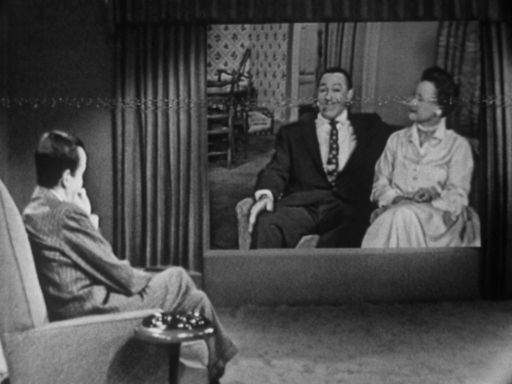 Newsman Edward R. Murrow is seated and looks at a screen projection of Cab Calloway and his wife ‘Nuffie,’ as he interviews both