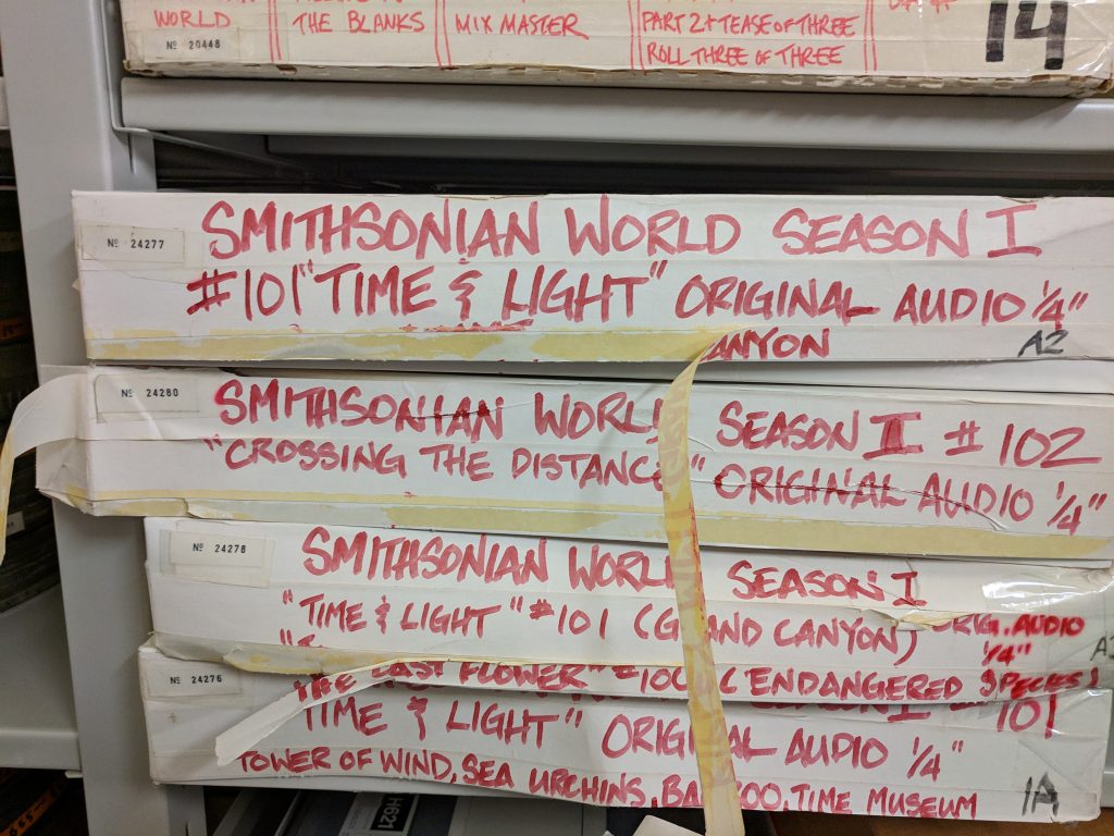 Cardboard boxes with red marker labeling containing audiovisual media elements for program called, Smithsonian World.