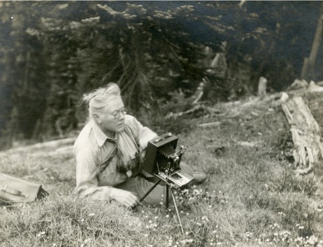 Woman with camera sits in grass.