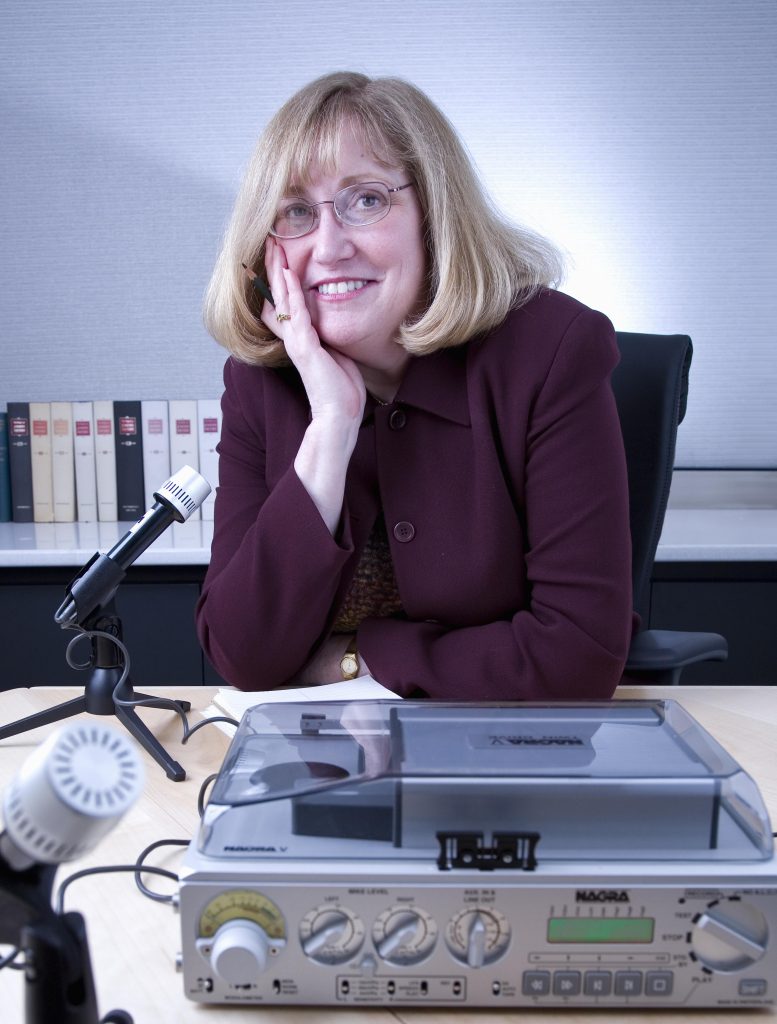Pamela Henson sits at a desk with a microphone and recording equipment.