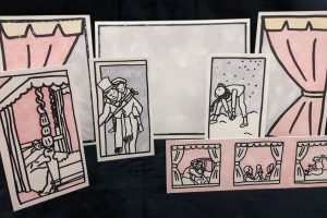 Mounted, standing prints of scenes from A Christmas Carol, in front of prints of a stage. 