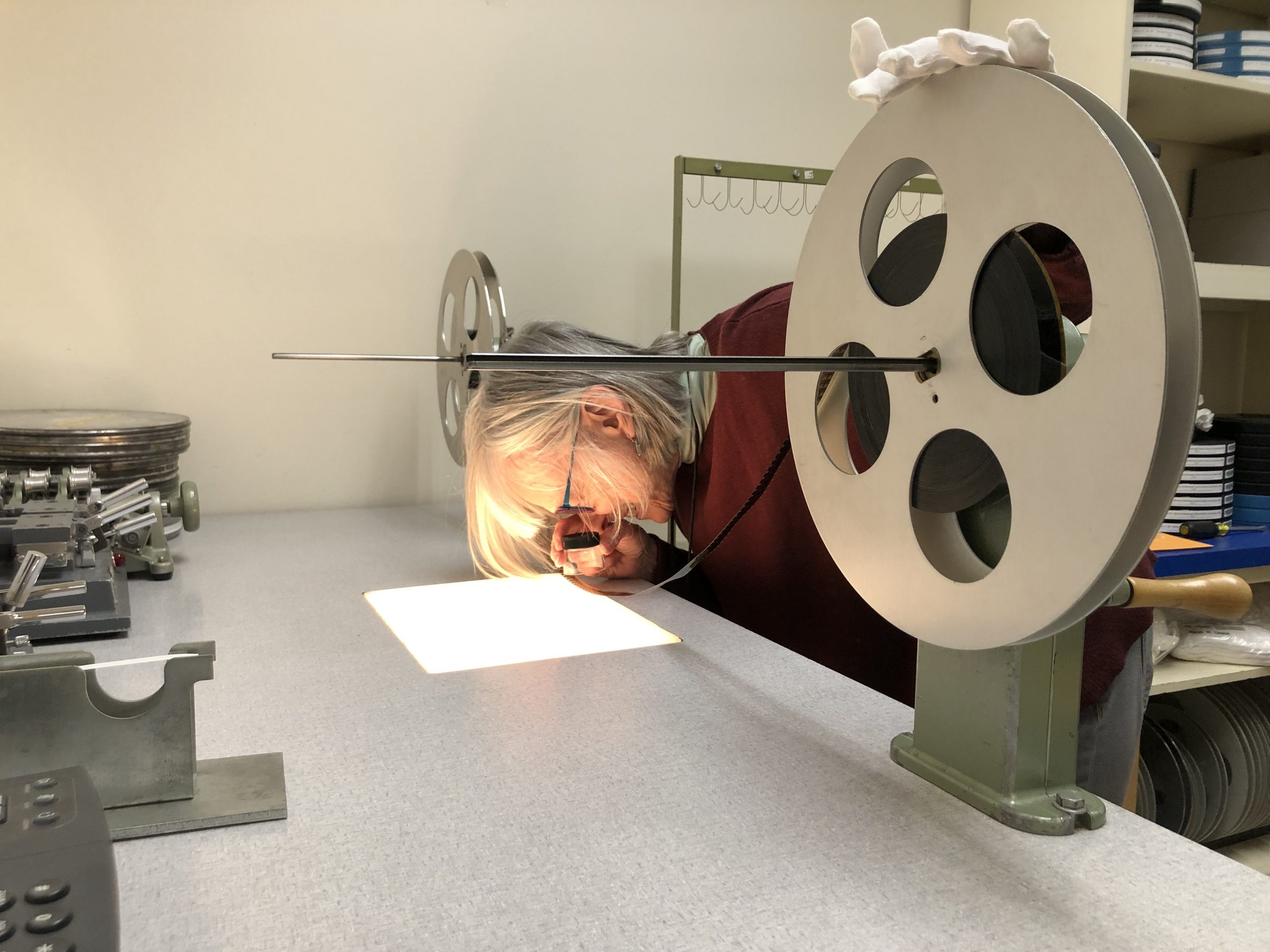 Smithsonian Film Archivist Pam Wintle closely inspects a 16mm film through a magnifying loupe lens over a light box.