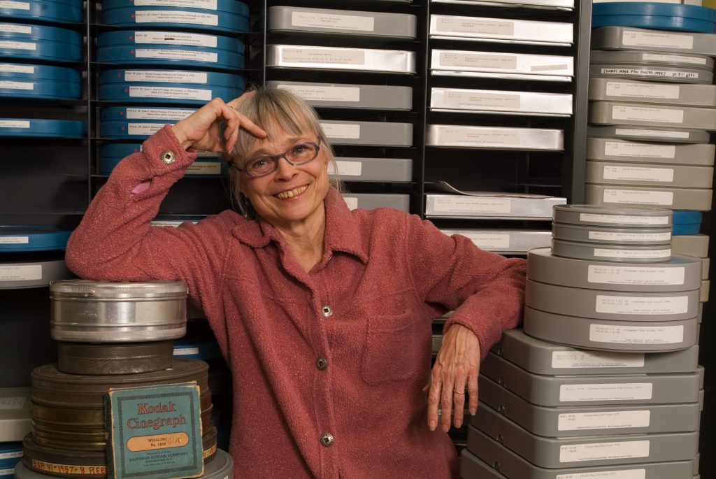 Film Archivist Pam Wintle stands against a backdrop of stacked cans and boxes of motion picture film.