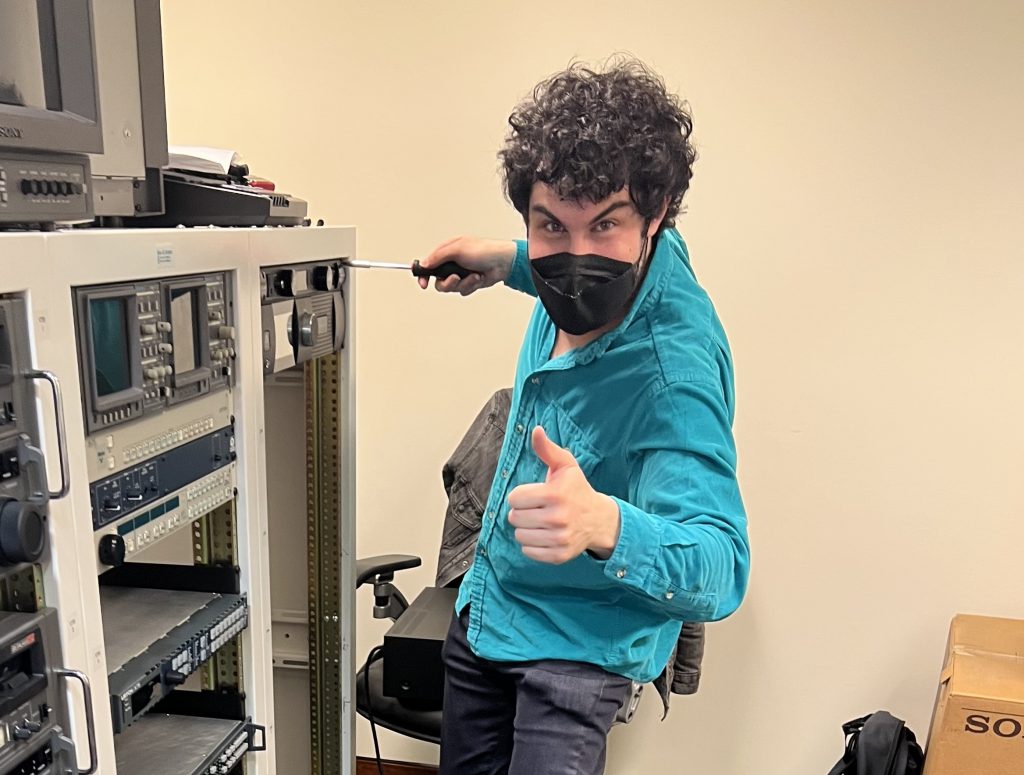 Dan Hockstein holds a screwdriver next to an audio rack. 