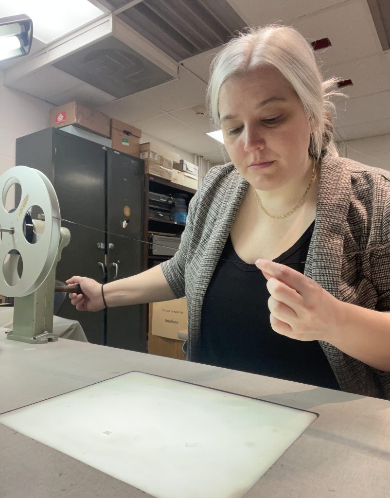 Analiese Oetting holds a strand of 16 mm between her fingers, inspecting the film on a rewind bench.