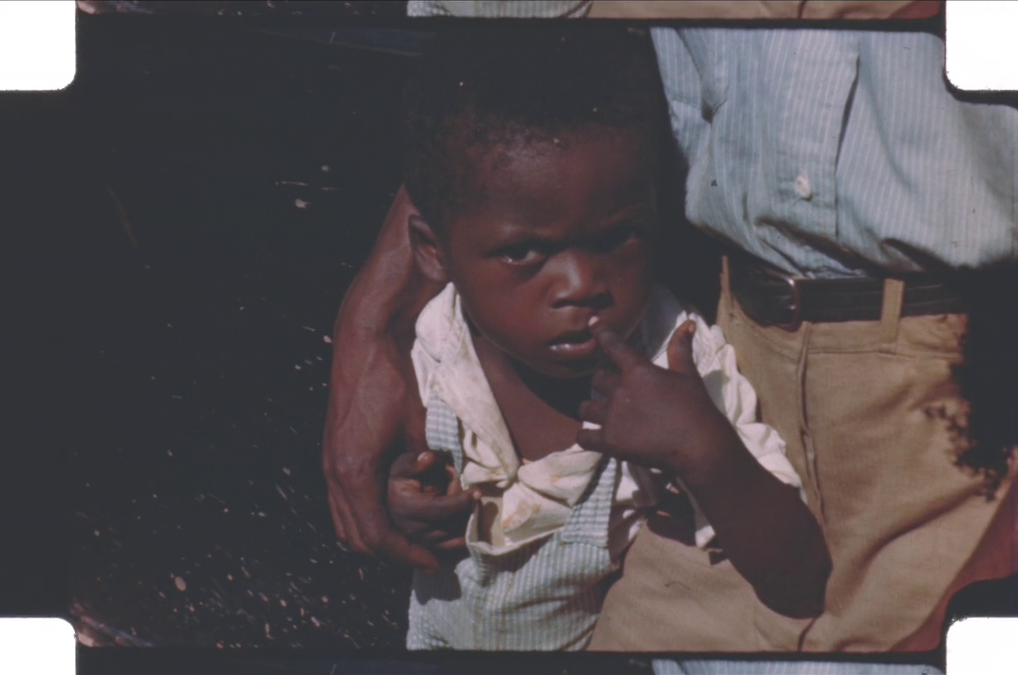 A young child, held by an adult, looks quizzically at the camera